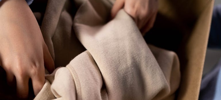 A person placing a sweater in a box for storing away winter clothes