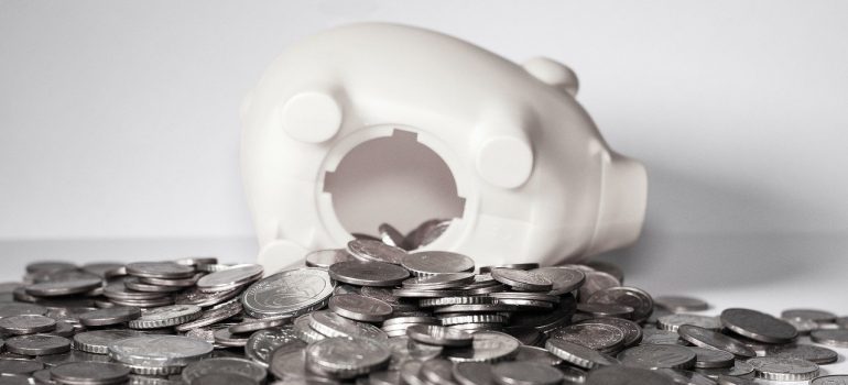 A white piggy bank with coins spilling out of it.