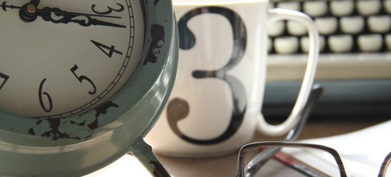 A close up of an alarm clock, a mug, and glasses.