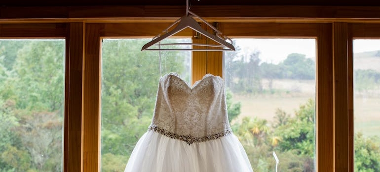 Elegant bridal dress hanging on window before packing and storing a wedding dress