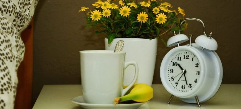 An alarm clock next to a pot and a cup.