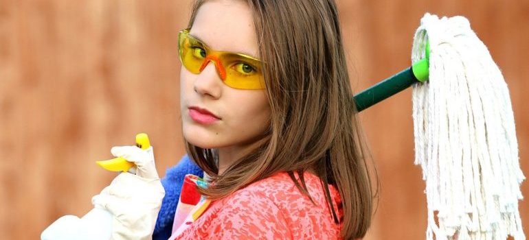 A girl holding a mop ready to clean before she goes to store a mattress.