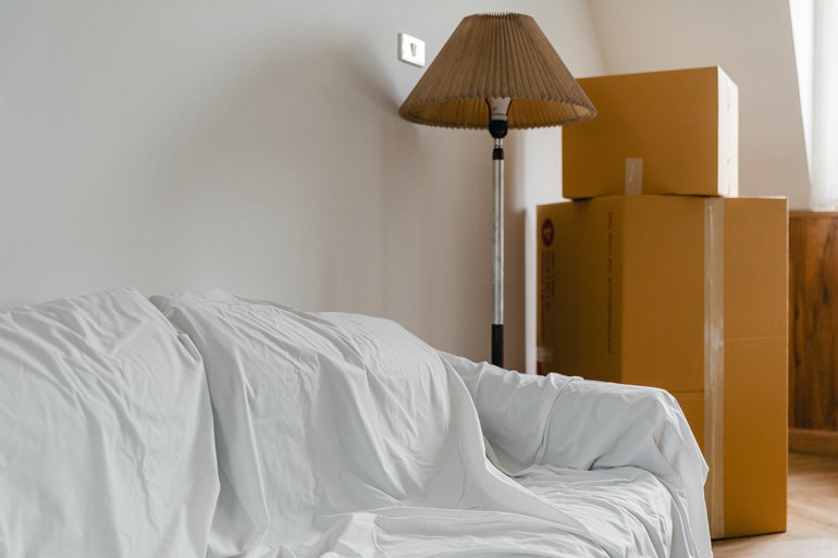 A sofa, lamp, and cardboard boxes covered with white cloth.