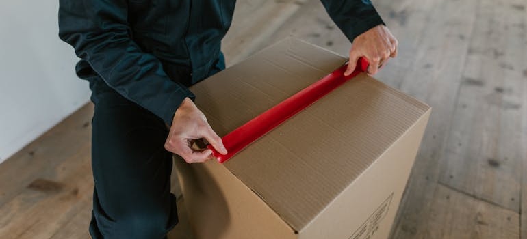 A man taping a box with a tape as one of the must-have self storage supplies