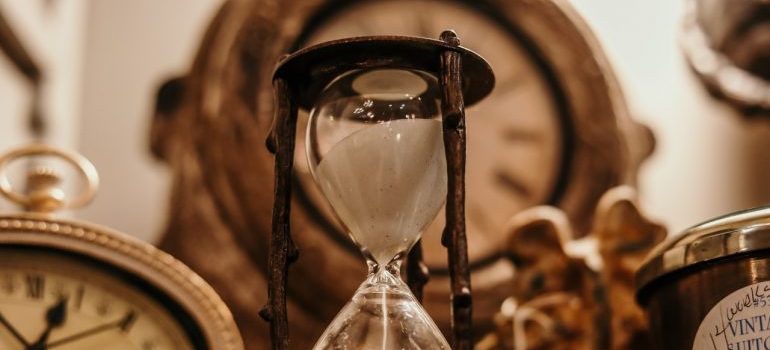An old hourglass in front of an antique clock.