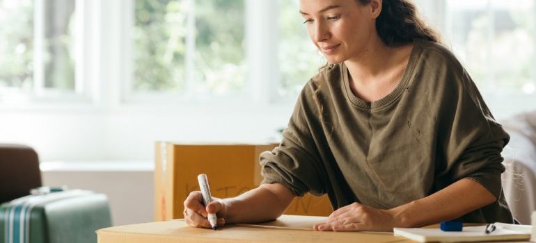 A woman labeling a cardboard box.