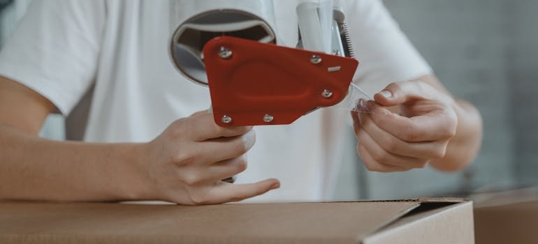 A person holds a red, packing tape dispenser.