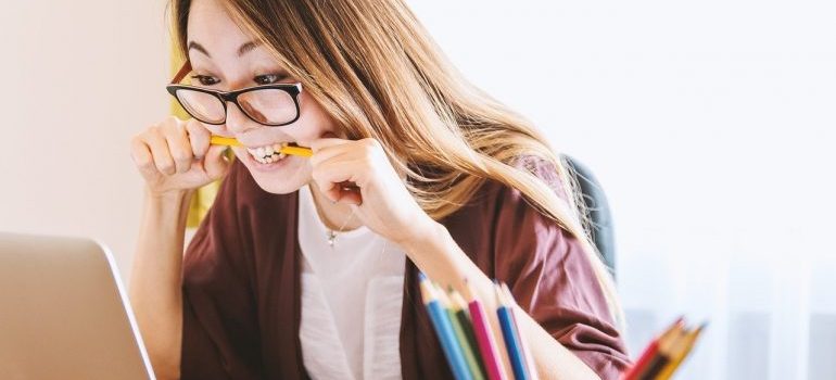 A woman biting a pen in front of a laptop.