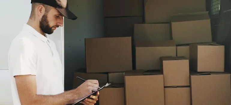 A man in front of boxes writes how self storage saves you money when moving interstate