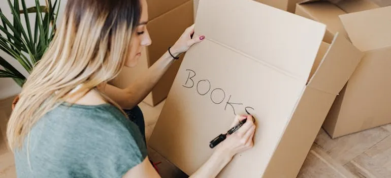 A woman labeling a box 'books'.