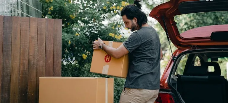 Young man taking boxes out of a car trunk.