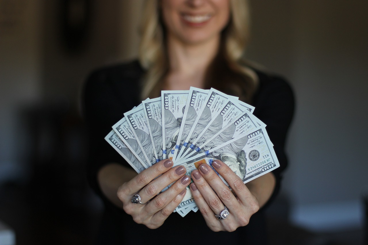 A smiling woman holding a fan of 100 dollar bills