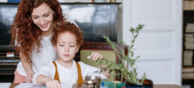 The mother holds the child in her arms and helps him organize things on the table – the way to help your child get organized.