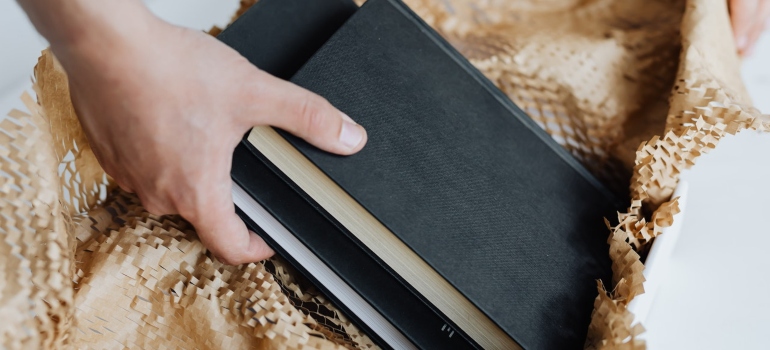 a hand putting books into paper and a cardboard box