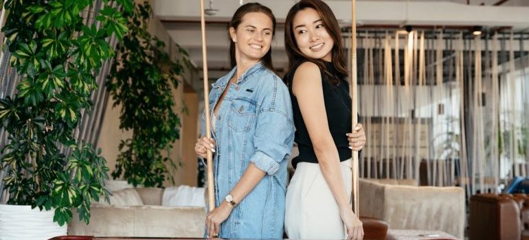 Two women smiling and standing by their pool table