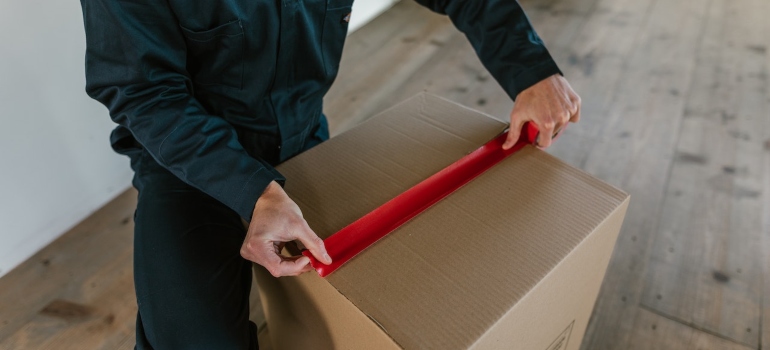 hand putting tape over a cardboard box is how to pack your Kenmore home during one weekend