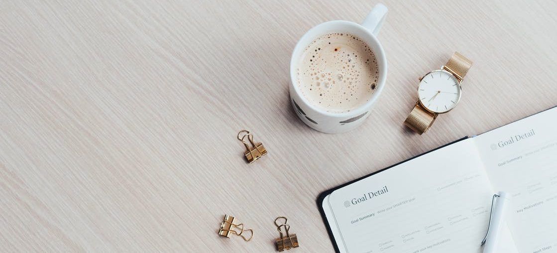 A to-do planner, a wristwatch, and a coffee mug on a table