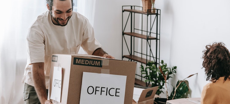 A man is moving boxes labeled Office because of the advantages of a minimalist office layout in Seattle.
