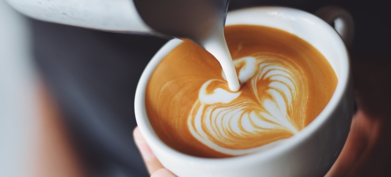 a person pouring milk into a cup of coffee