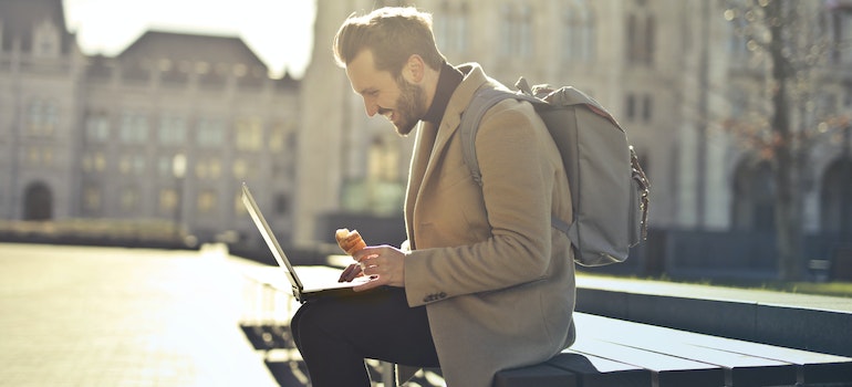 A man with a backpack is typing on his laptop