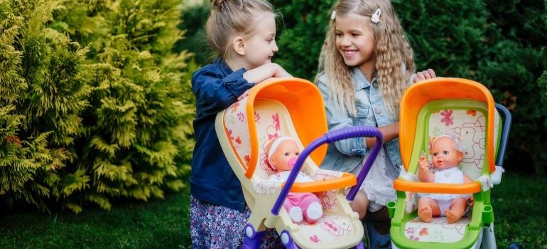 Two girls pushing the baby strollers with dolls inside