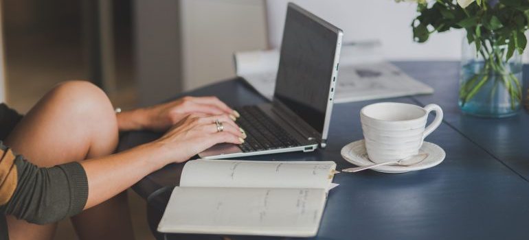 Person typing on laptop, notebook and mug on the table next to it