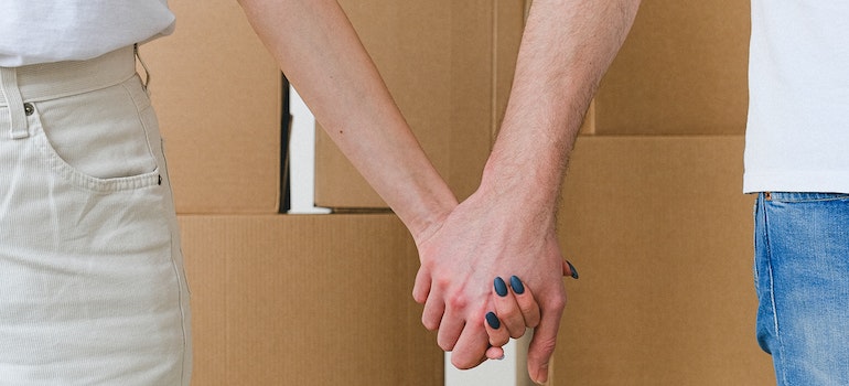 Crop couple holding hands near stack of cardboard boxes
