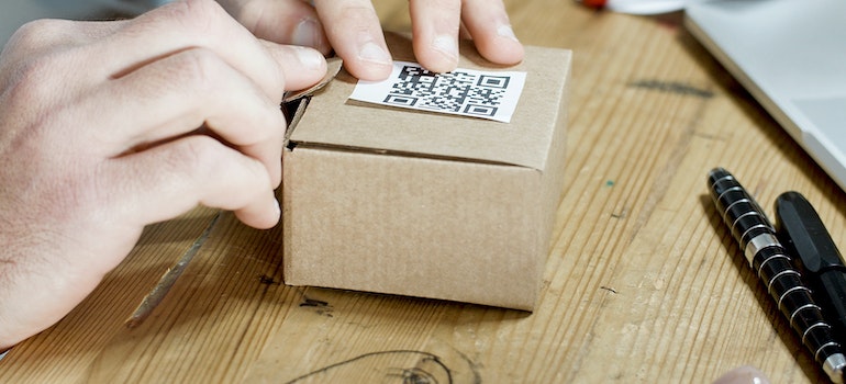 Person sticking a QR code to a Brown Cardboard Box