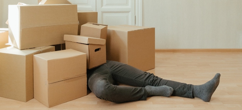A person in black pants lying under brown cardboard boxes during home remediation projects