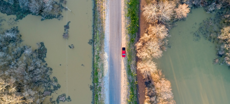 Red truck parked on side of road while the driver observes muddy flood waters.