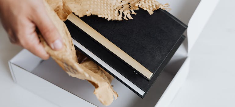 Anonymous man wrapping pair of black notebooks in packing paper