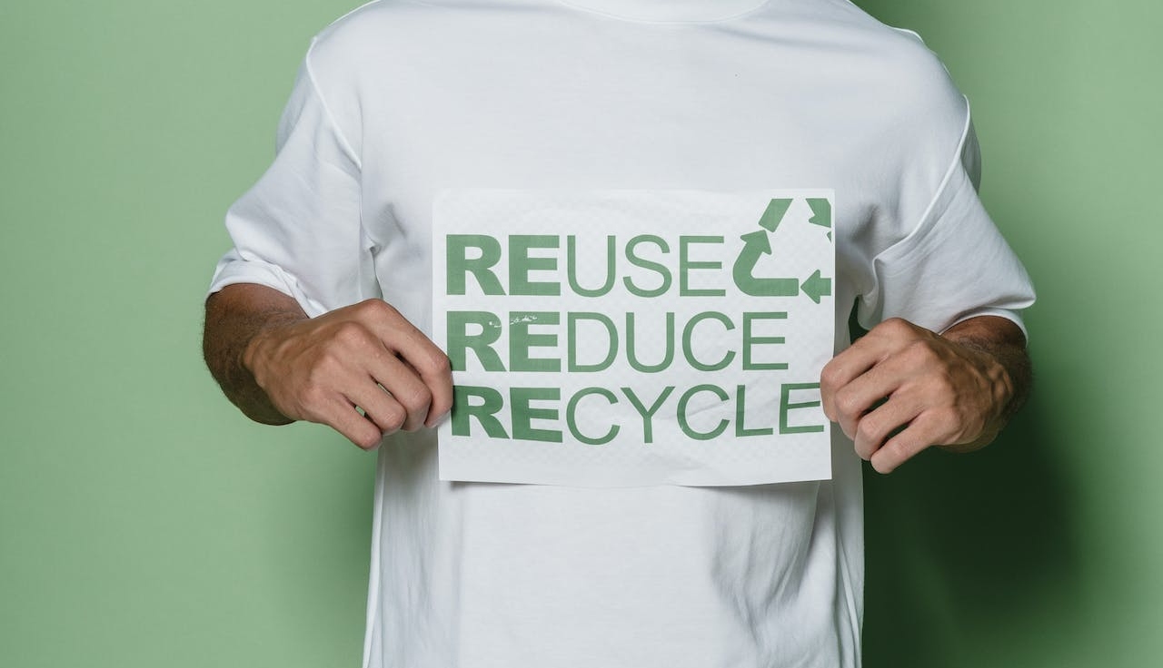 Man in white and green crew neck t-shirt holds a 3R sign