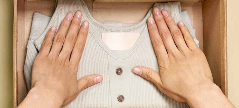 A Person packing a sweater in a Brown Cardboard Box