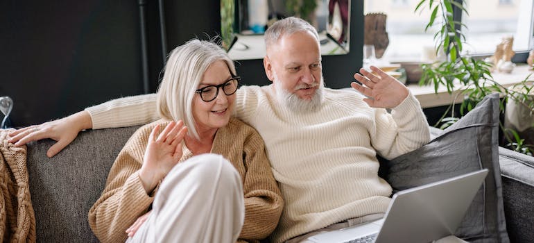 Elderly couple sitting on the sofa waving on a video call after downsizing during the festivities