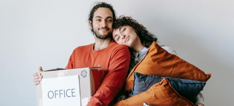 Man Carrying A Box And Woman With Throw Pillows In A Basket