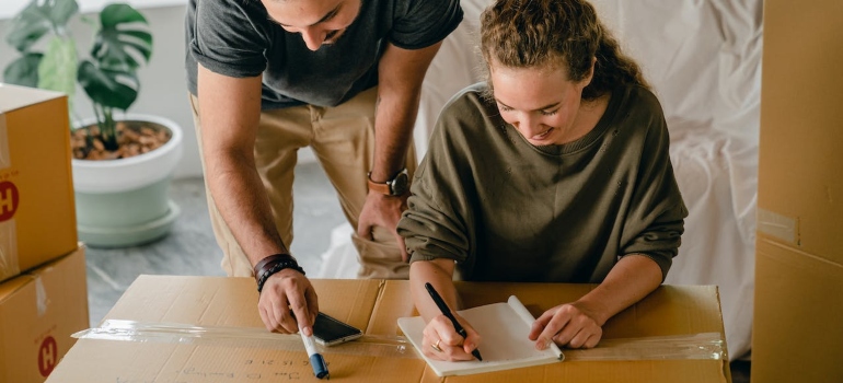 couple writing in notebook near boxes before relocation