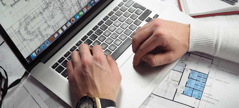 Man Using Turned-on Macbook Pro on White blueprint Papers