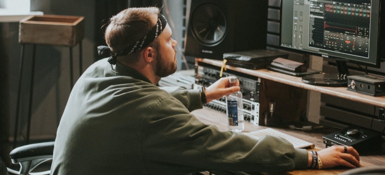Young bearded man in hairband sitting at desk in home music studio
