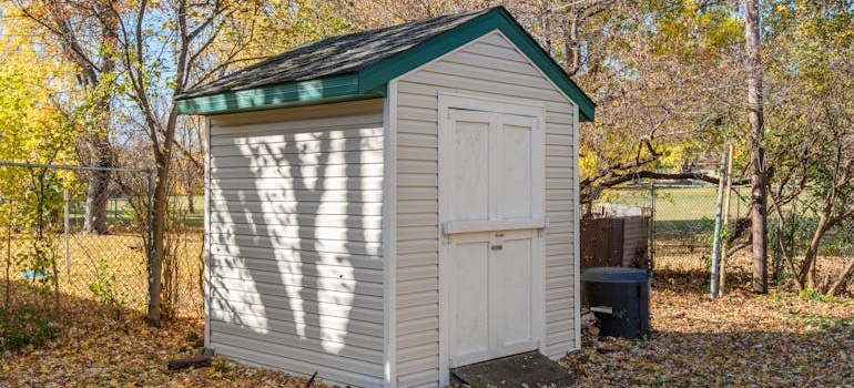 An outdoor storage shed near trees and fallen leaves during fall.