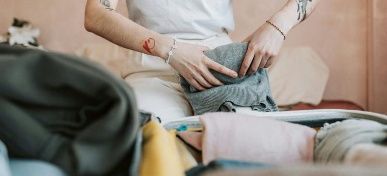 Person sitting and folding clothes after learning how to utilize storage services