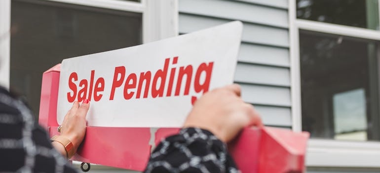 Person holding a signage sale pending outside a house