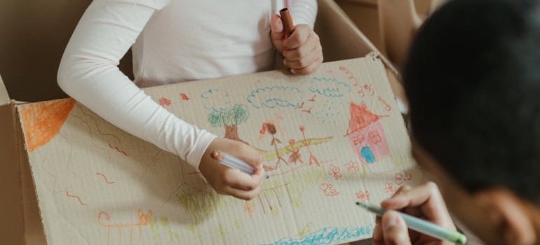 A kid and a father are reusing leftover packing materials by drawing on a box