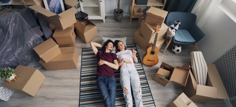 Couple lying down on carpet amid boxesand a guitar
