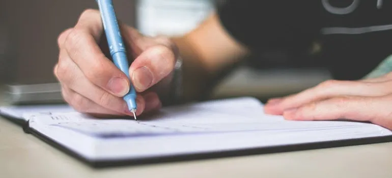 Person holding blue ballpoint pen writing in notebook