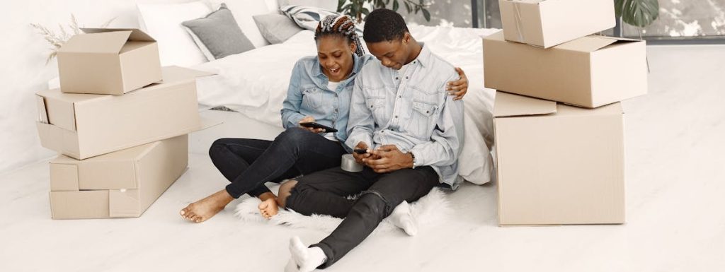 A young couple using their smartphones while sitting amid boxes.